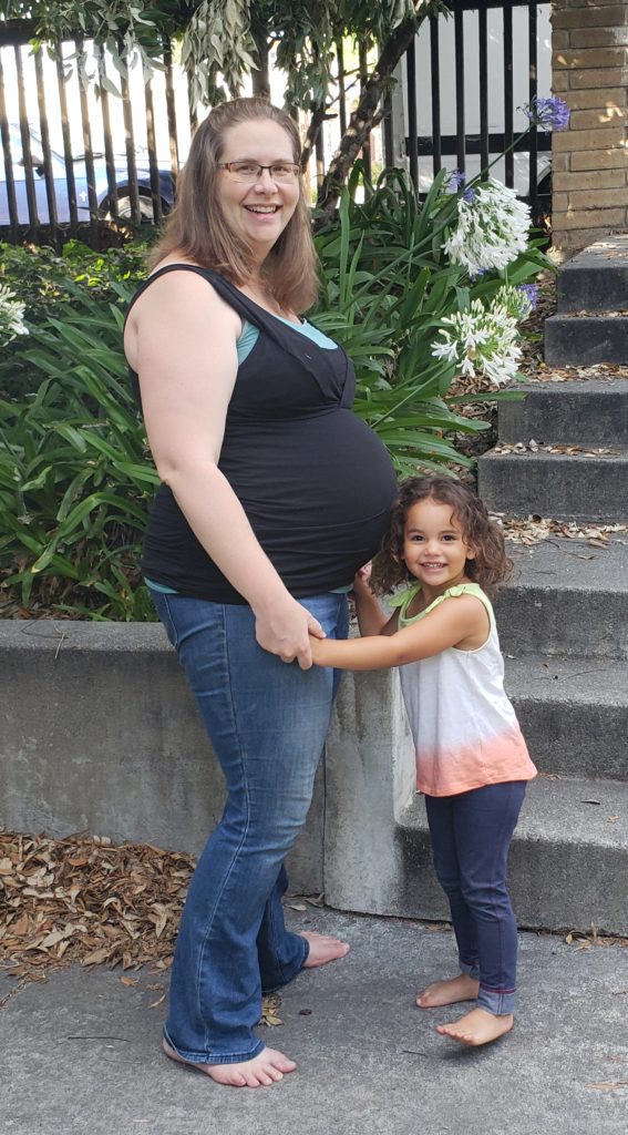Side shot of Tromila nine months pregnant with Finiasi and Ana Lia at 3 years old is standing beside her smiling. Both are barefoot.