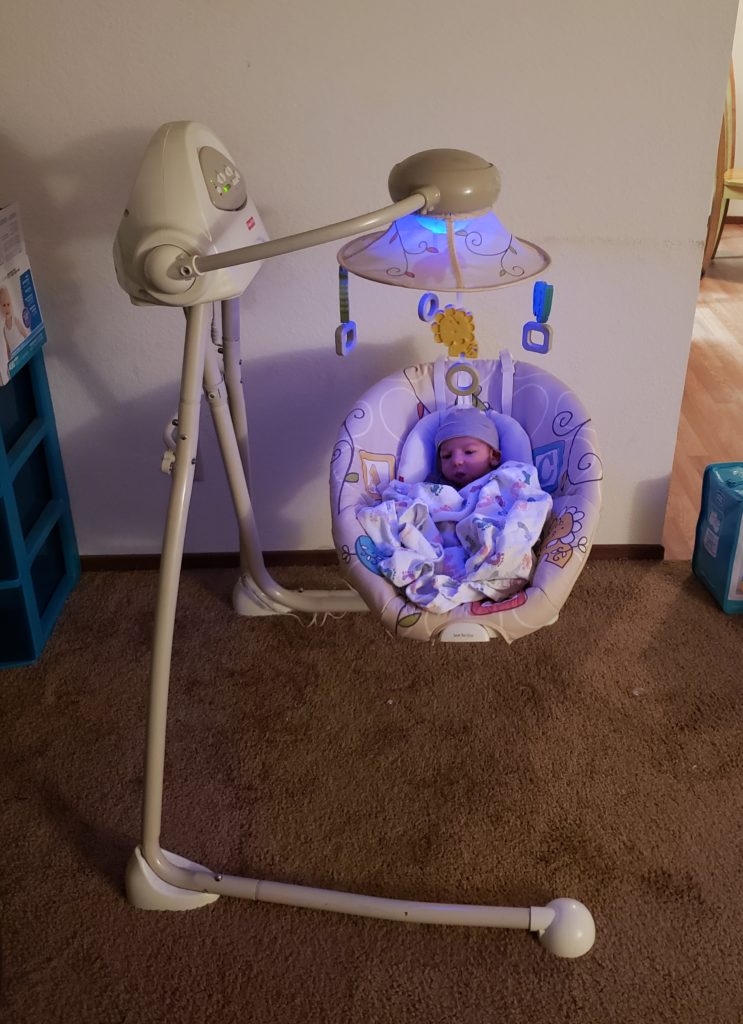 Fin as a newborn in an electric baby swing with a blue light shining on him