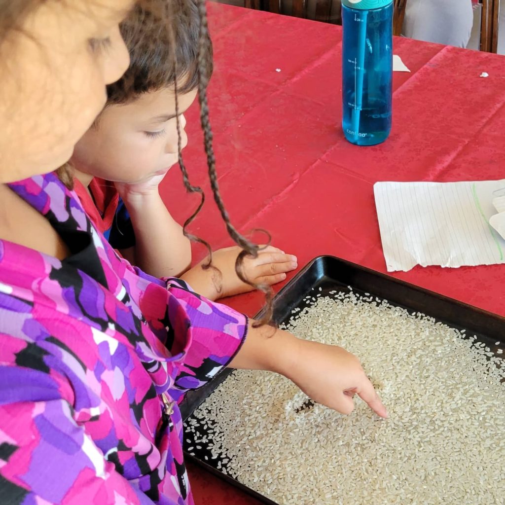 two kids writing in rice on a pan