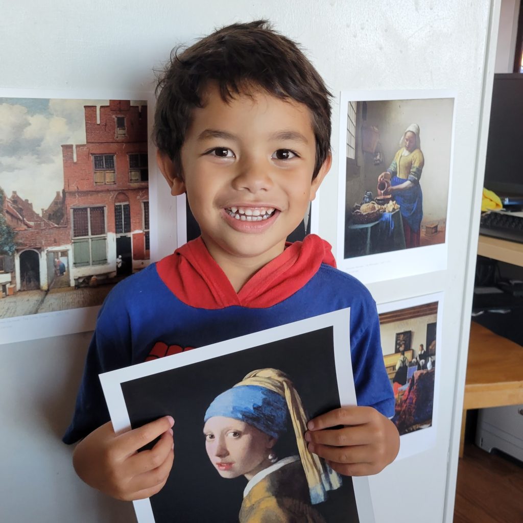 boy holding Vermeer print with 5 others on the wall behind him
