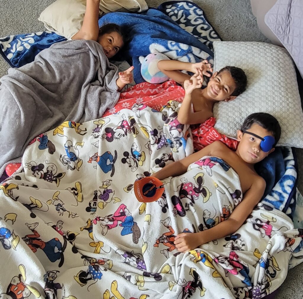 three kids on floor wrapped in blankets