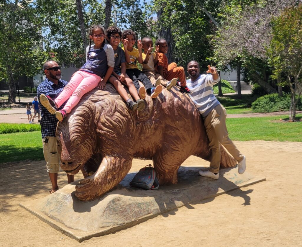 four kids and two adults beside giant sloth statue